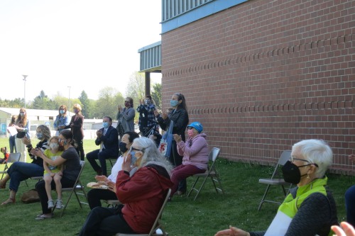 Crowd of adults and children in the shade of brick building